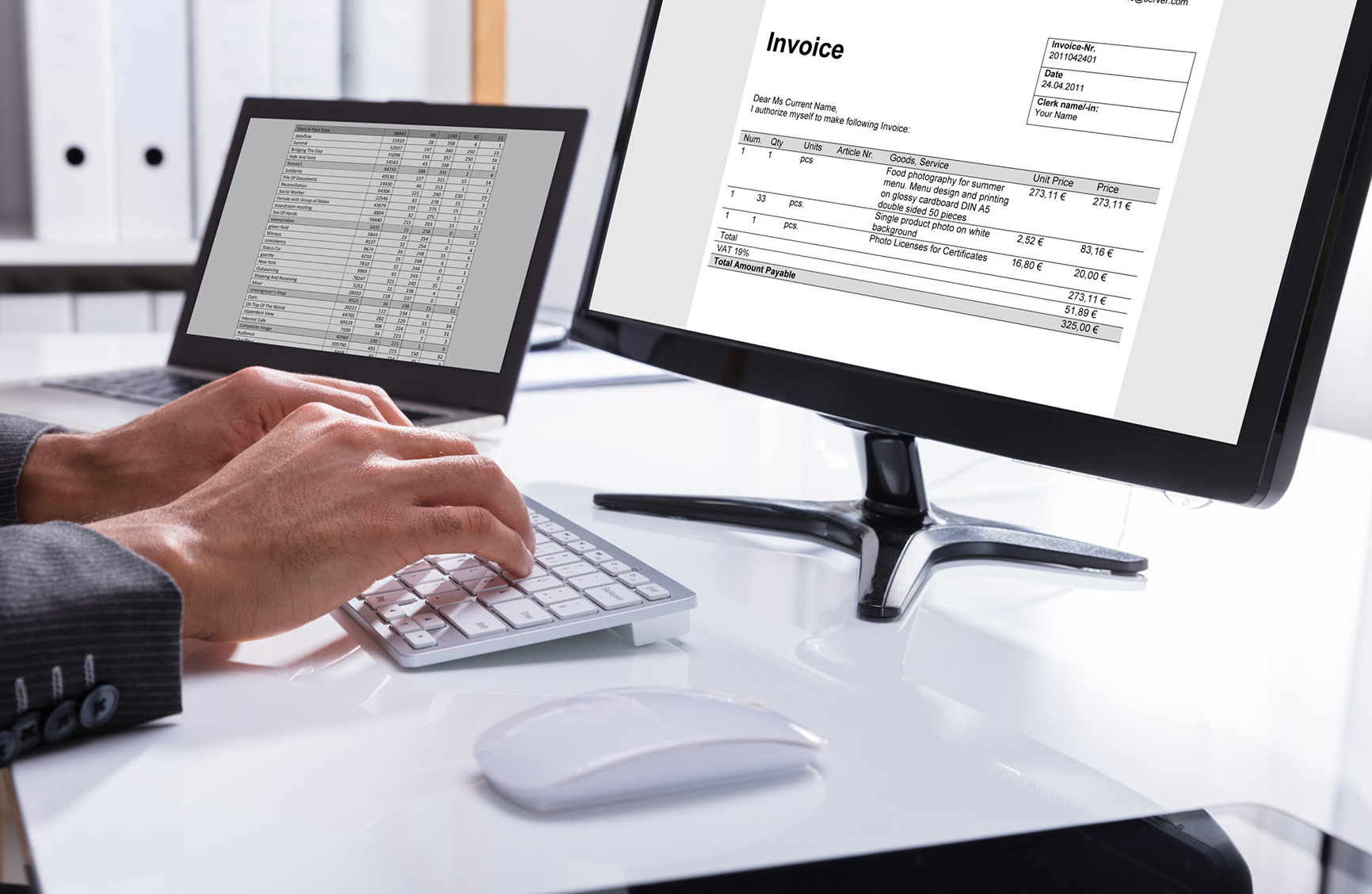 Person typing on a keyboard with an invoice document displayed on a computer monitor.