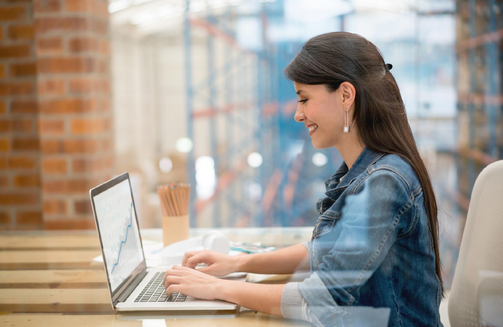 Woman working on a laptop in an office, smiling as she types.