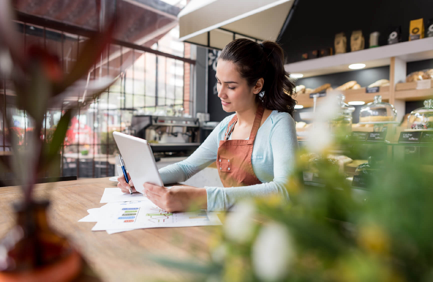 Young woman in a café working on a tablet and reviewing charts.