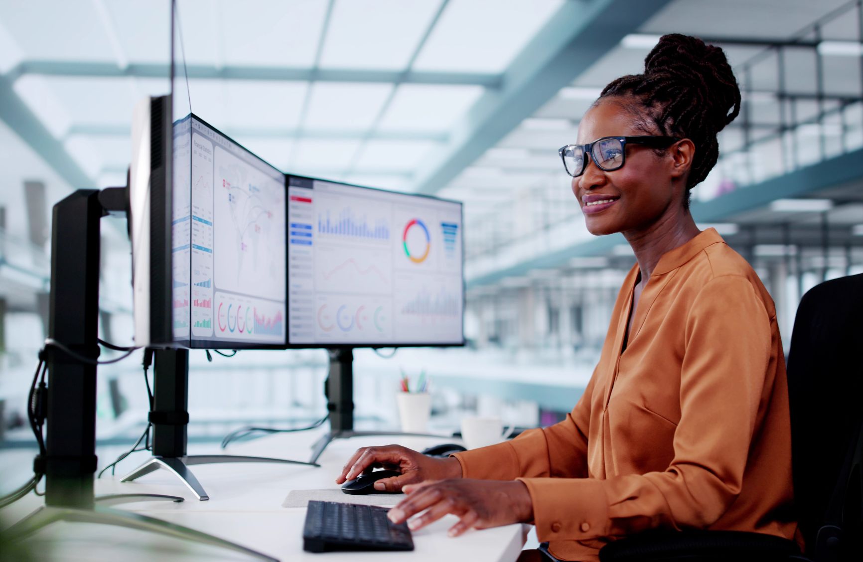 Woman looking at three computer screens with graphs on them.