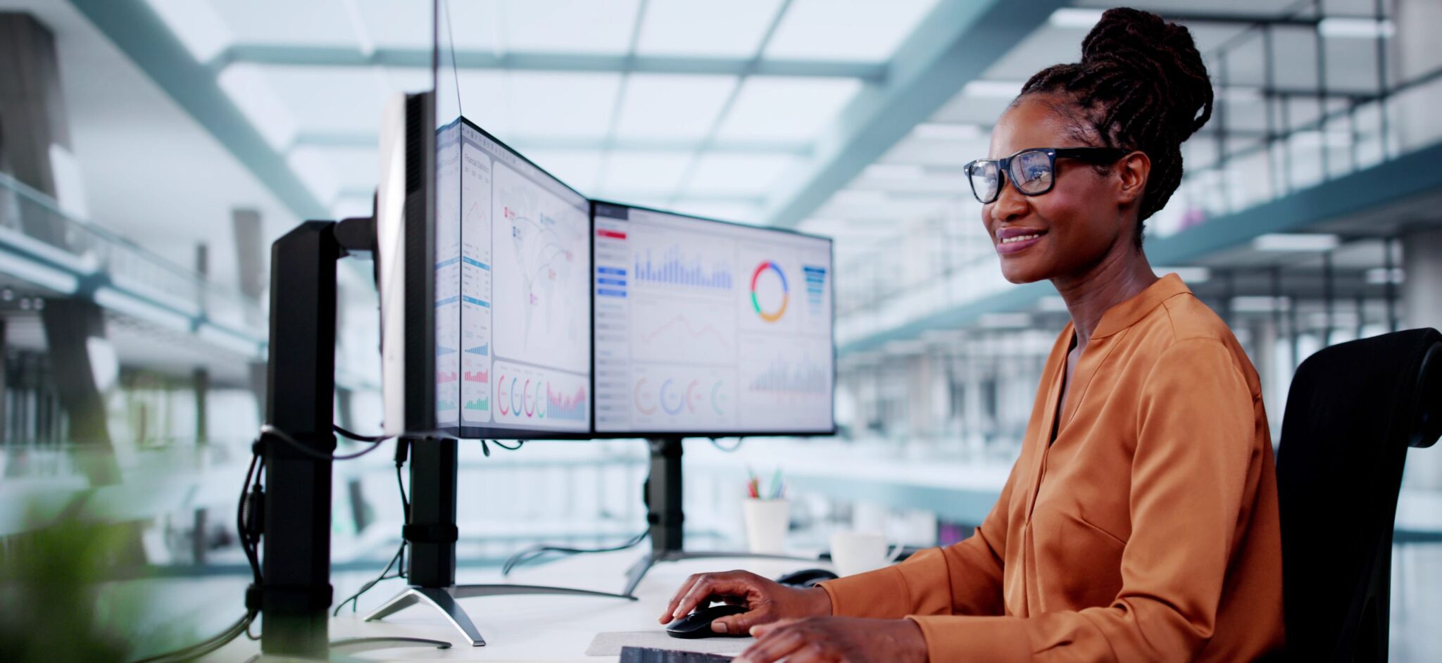 Woman looking at three computer screens with graphs on them.